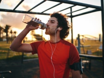 Um homem bebe água durante o exercício para garantir a hidratação