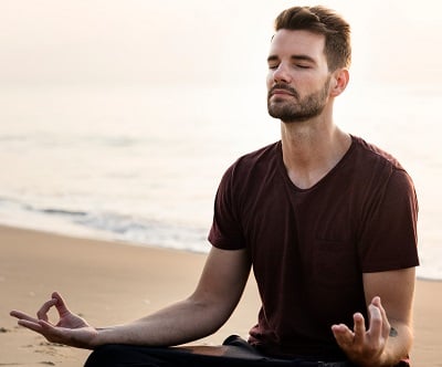 Ein gut aussehender Mann praktiziert Yoga am Strand