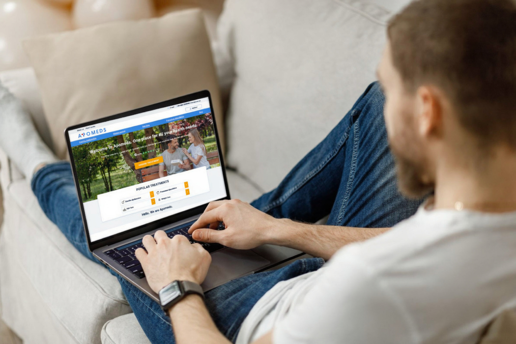 A man sitting on a couch, using a laptop on his lap, focused on the screen in a cozy living room setting.