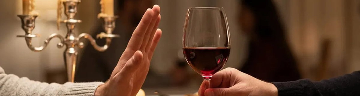Eine Handlehnt ein Glas Rotwein bei einem romantischen Abendessen bei Kerzenschein ab