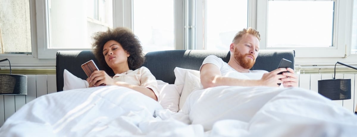 Ein Mann und eine Frau liegen mit ihren Handys im Bett