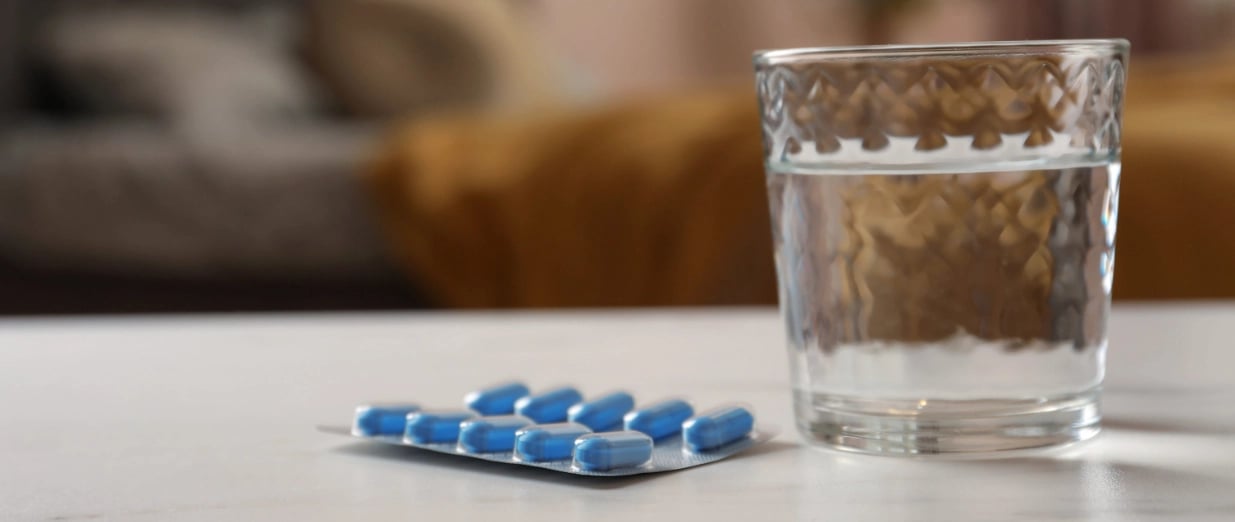 A glass of water beside a blister pack of blue pills on a table