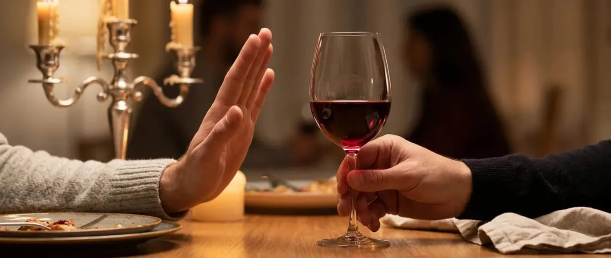 Eine Handlehnt ein Glas Rotwein bei einem romantischen Abendessen bei Kerzenschein ab