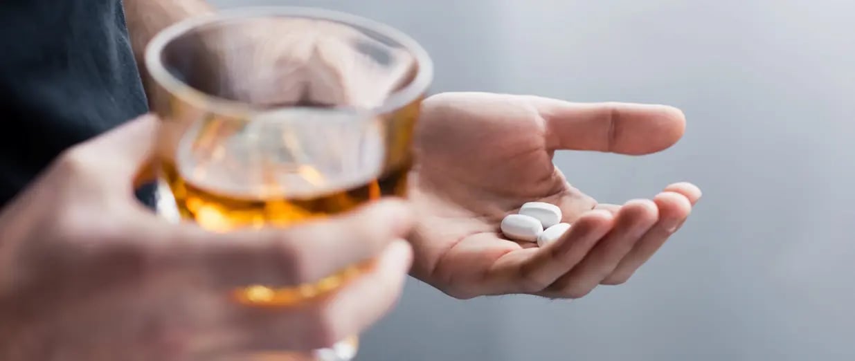 Person h&auml;lt Tabletten und ein Glas Alkohol in der Hand