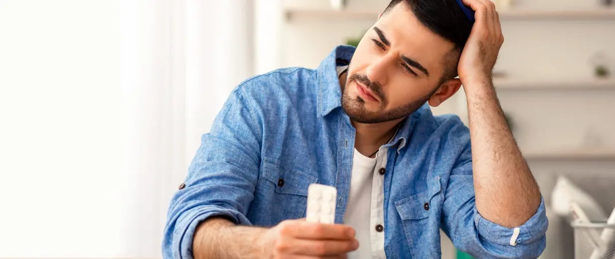 Homem pensativo segurando um medicamento