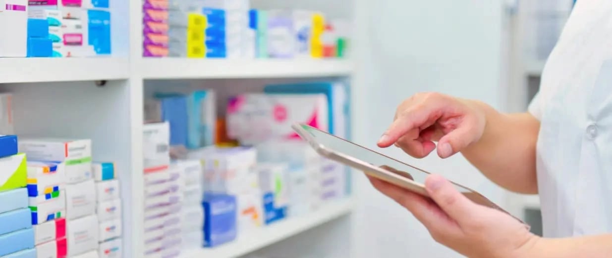 Profissional de sa&uacute;de usando um tablet para verificar o estoque de medicamentos em prateleiras de uma farm&aacute;cia