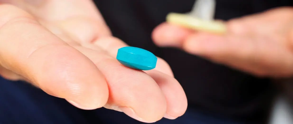 Hand h&auml;lt eine blaue Tablette und ein Kondom