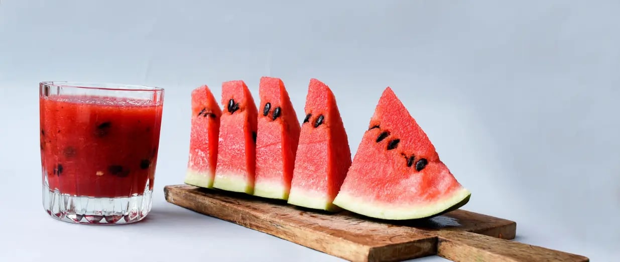 Watermelon slice on a wooden board with juice on a gray background