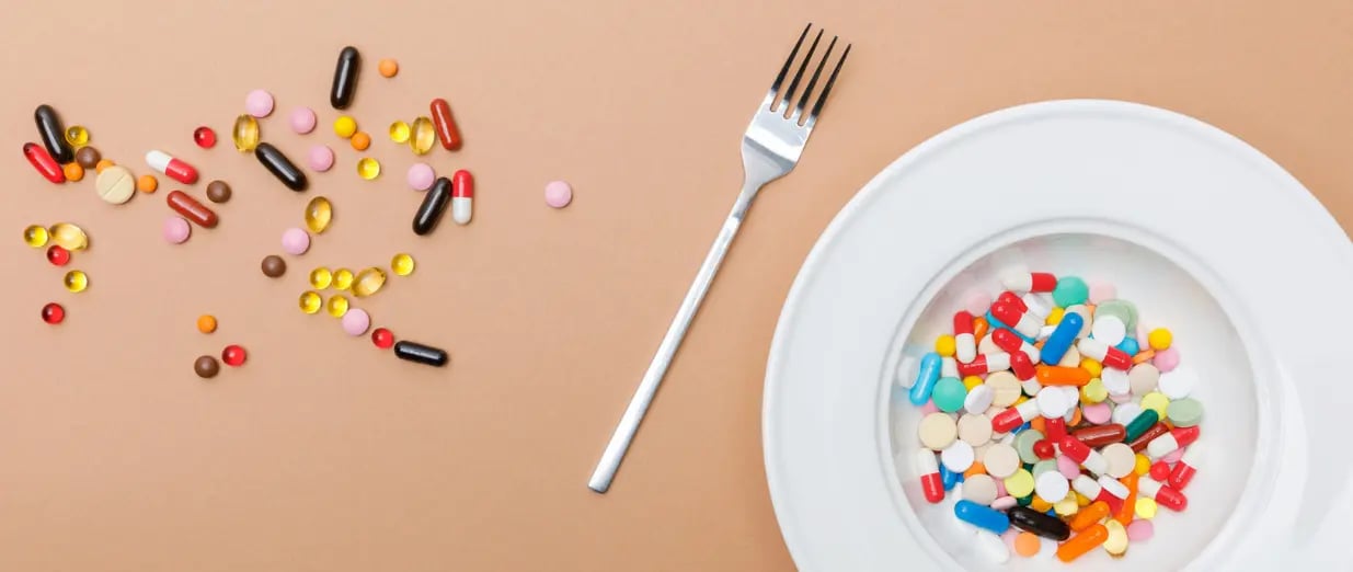 Bunte Tabletten und Kapseln auf einem Teller mit Gabel daneben