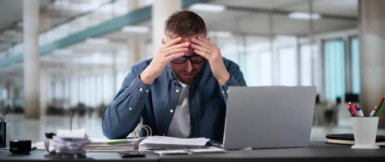 Ein gestresster Mann sitzt im B&uuml;ro und h&auml;lt sich den Kopf