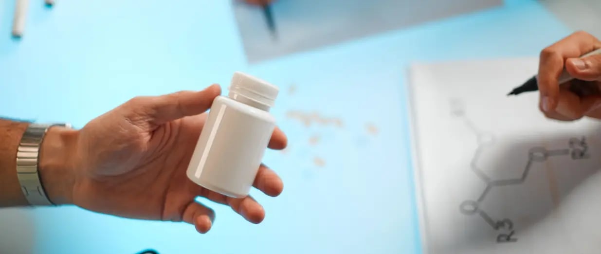A hand holding a pill bottle next to a chemical diagram being drawn