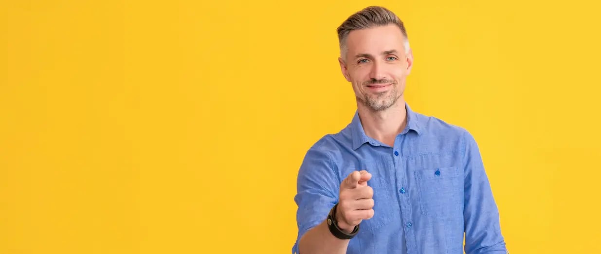 A smiling man points directly at the camera against a yellow background