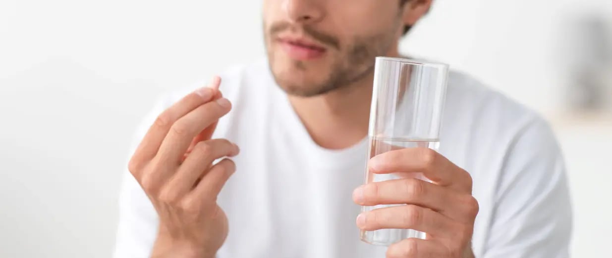 Mann h&auml;lt ein Glas Wasser und eine Tablette in der Hand