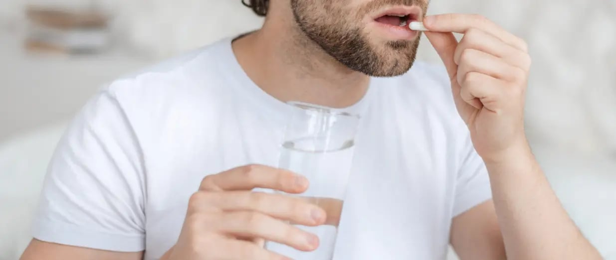 Mann nimmt eine Tablette mit einem Glas Wasser ein
