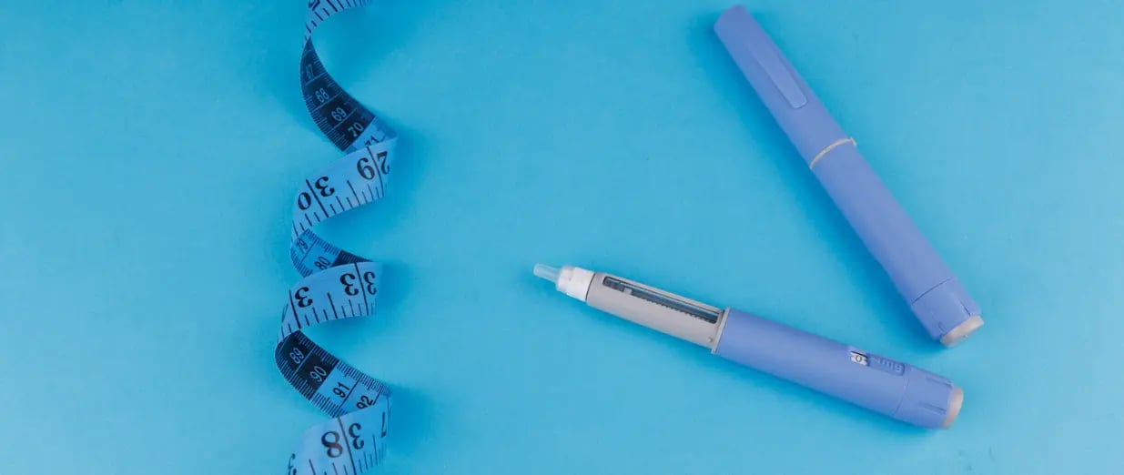 Zwei Injektionspens neben einem Ma&szlig;band auf blauem Hintergrund