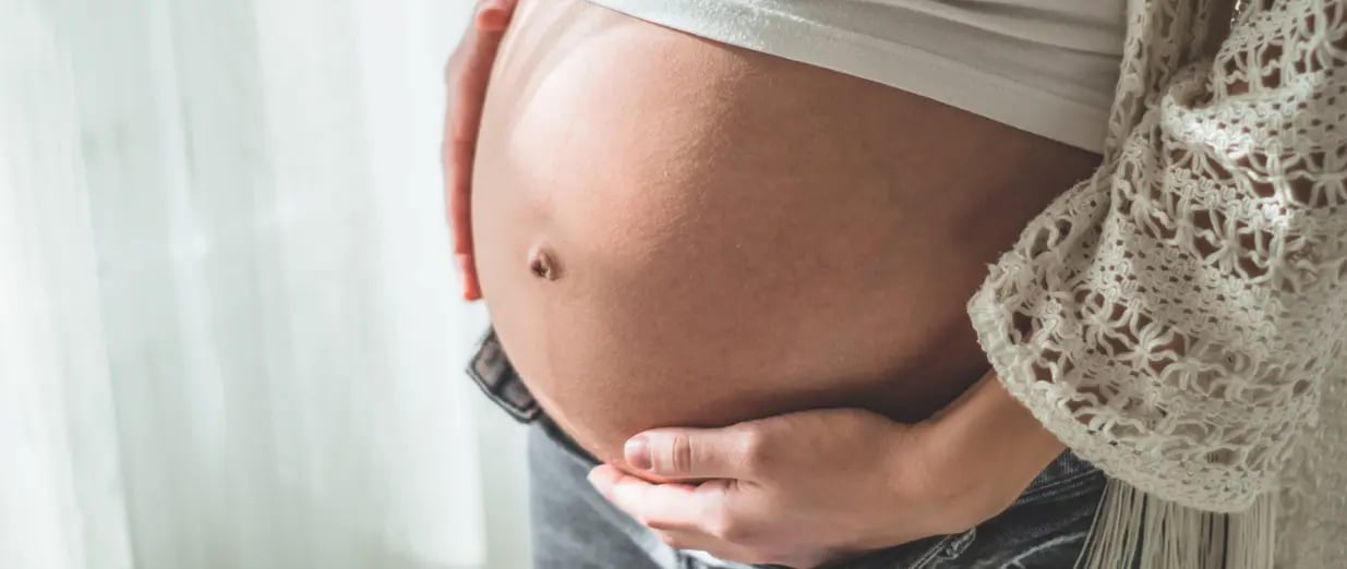 Schwangere Frau mit Babybauch bei Tageslicht