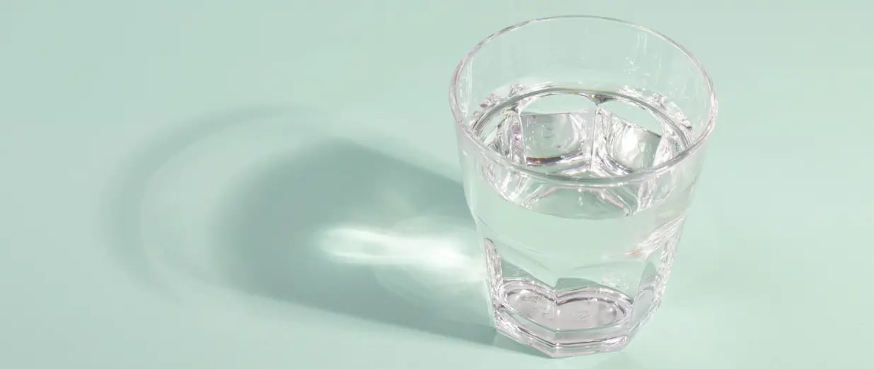 Ein transparentes Glas Wasser auf einer hellgr&uuml;nen Oberfl&auml;che mit Schattenwurf