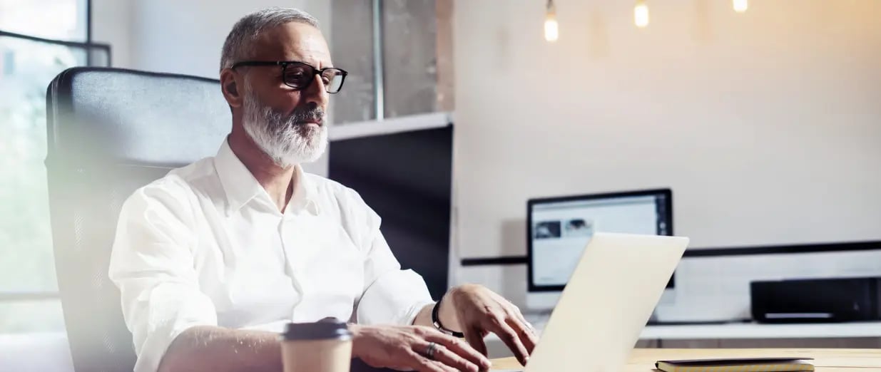 &Auml;lterer Mann mit Brille arbeitet an einem Laptop im B&uuml;ro