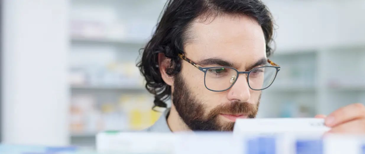 Homem analisando medicamento na farm&aacute;cia