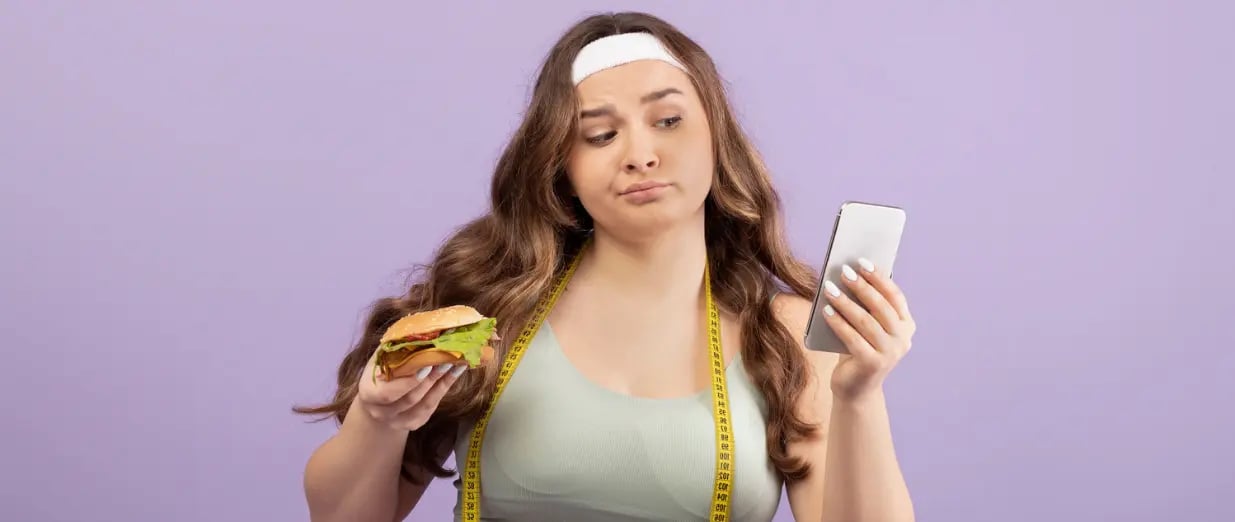 Eine Frau hält einen Burger und schaut auf ihr Smartphone