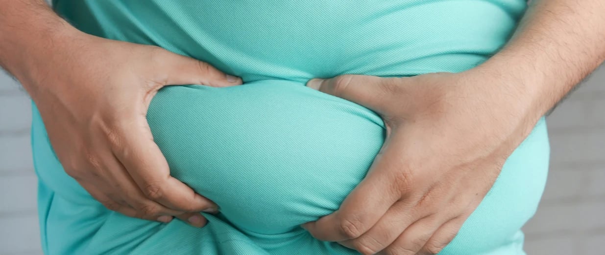 Übergewichtiger Mann in türkisfarbenem Hemd drückt sich den Bauch