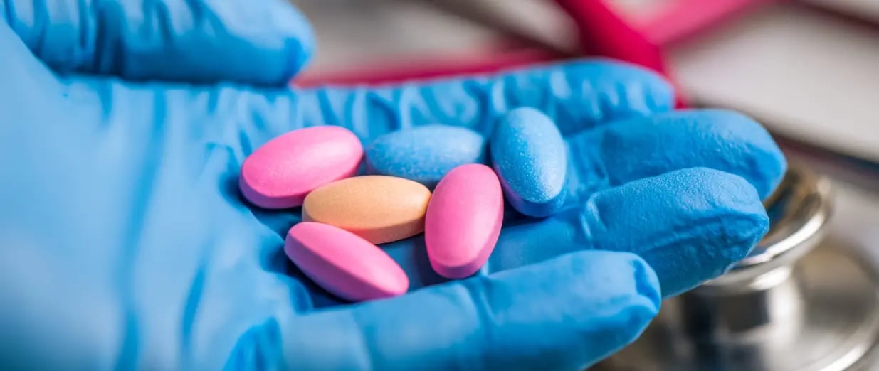 A gloved healthcare professional holds colorful medications