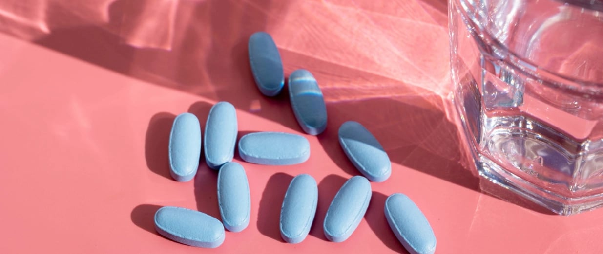 Blaue Tabletten neben einem Glas Wasser auf rosa Hintergrund