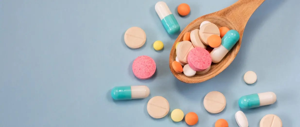Comprimidos e c&aacute;psulas variados em colher sobre fundo azul