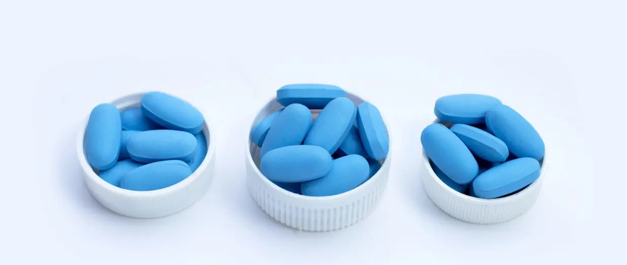 Blue Viagra tablets placed in small white caps on a light background