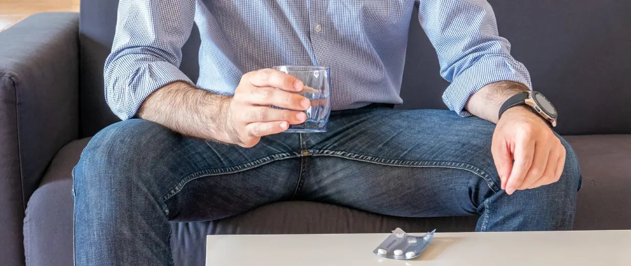 Mann mit Wasserglas und Tabletten auf dem Sofa