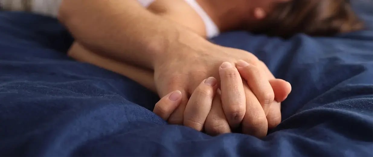 Zwei Personen halten sich im Bett an den H&auml;nden