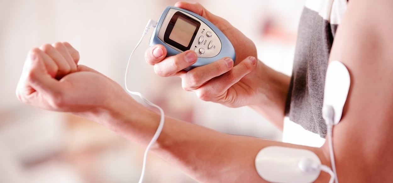Ein Mann mit einem Elektrostimulationsgerät in der Hand und mit Elektroden im Arm