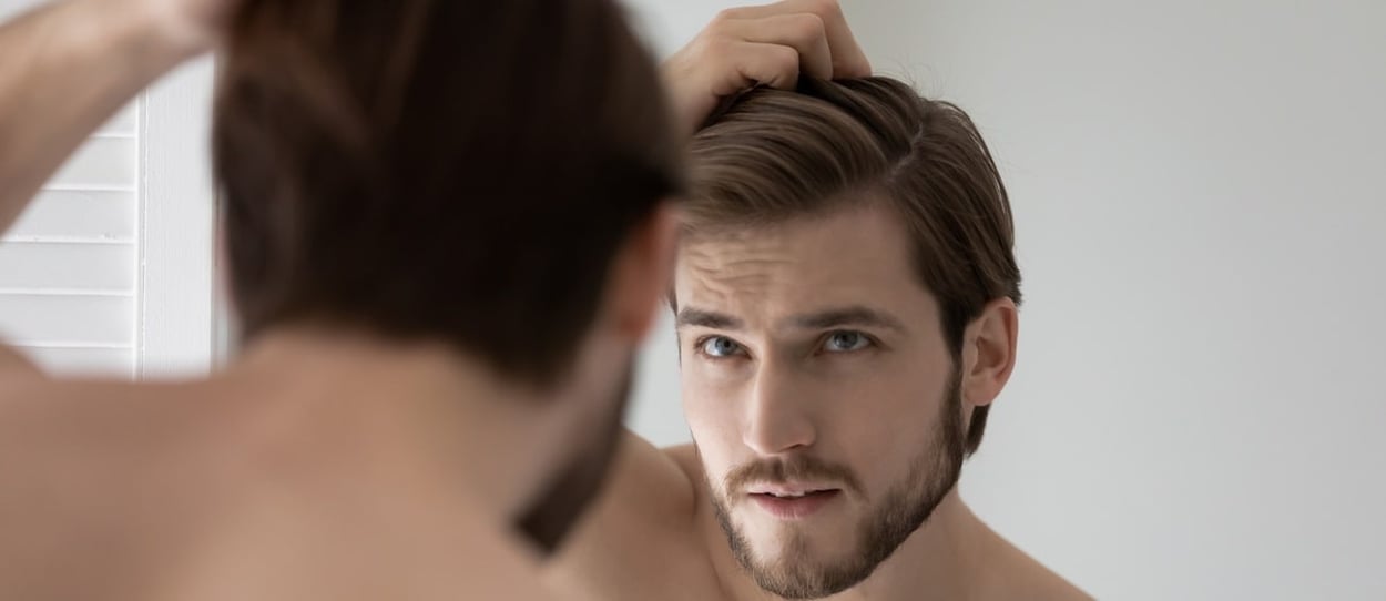 Ein Mann, der besorgt über seinen Haarausfall in den Spiegel schaut