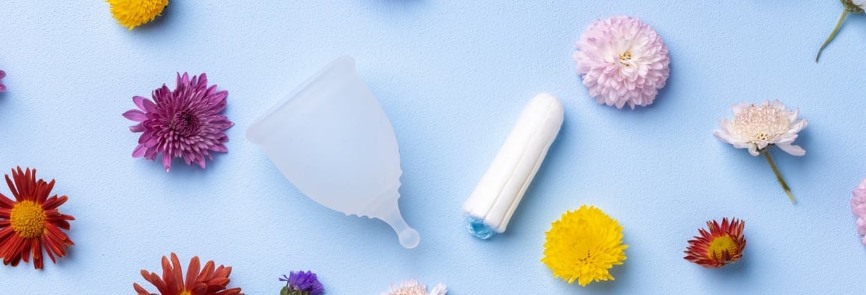 Menstruationstasse und Tampons auf Blumenmusterhintergrund