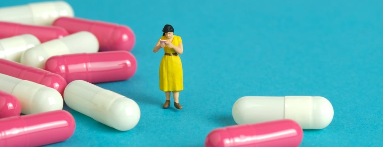 Eine Miniaturfrau steht neben einem Stapel Pillen.