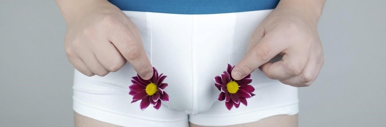 Homem de calças brancas segura flores como símbolo do cancro dos testículos