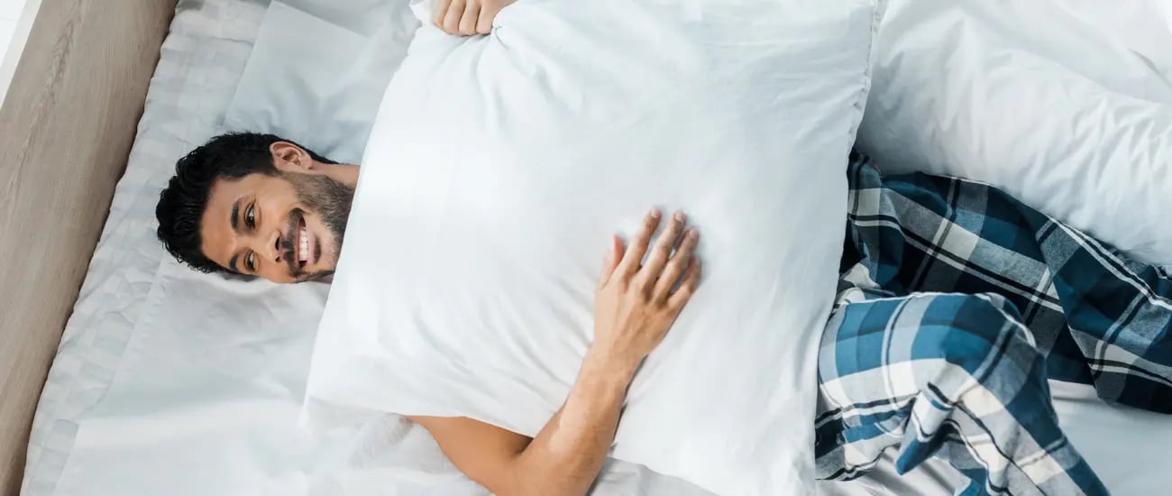 Ein gl&uuml;cklicher Mann liegt mit einem Kissen im Bett