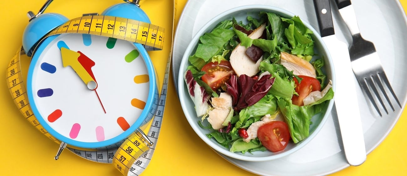 Ein Teller mit Salat, ein Wecker und ein Maßband als Konzept für eine Ernährungsstrategie