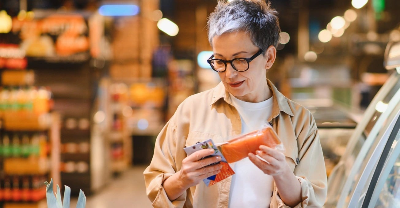 Eine Frau, die im Supermarkt sorgf&auml;ltig eine Lachsverpackung ausw&auml;hlt und sich bewusst f&uuml;r gesunde Lebensmittel entscheidet