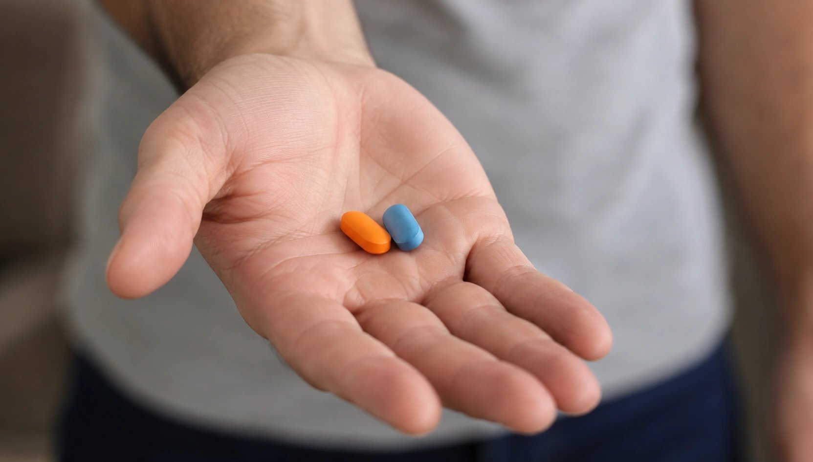 Man holds an orange tablet and a blue tablet in his open palm.