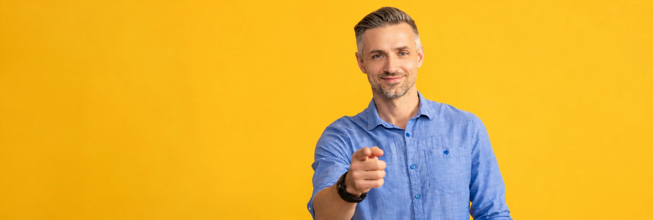 A smiling man points directly at the camera against a yellow background