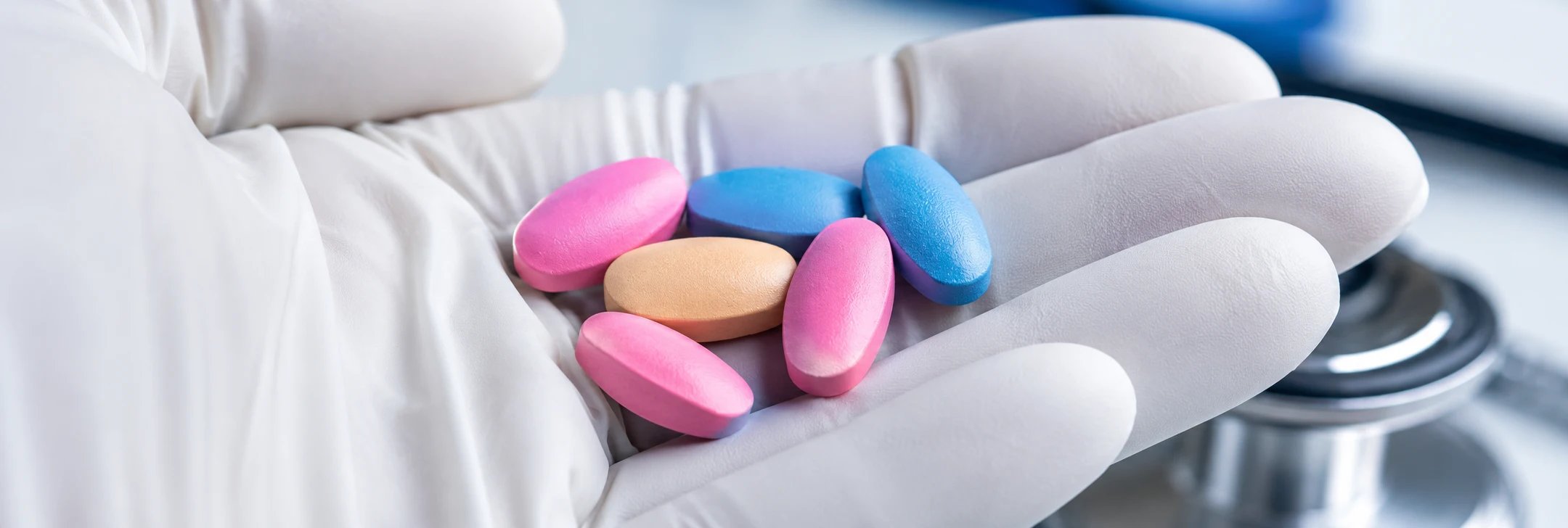 A gloved healthcare professional holds colorful medications