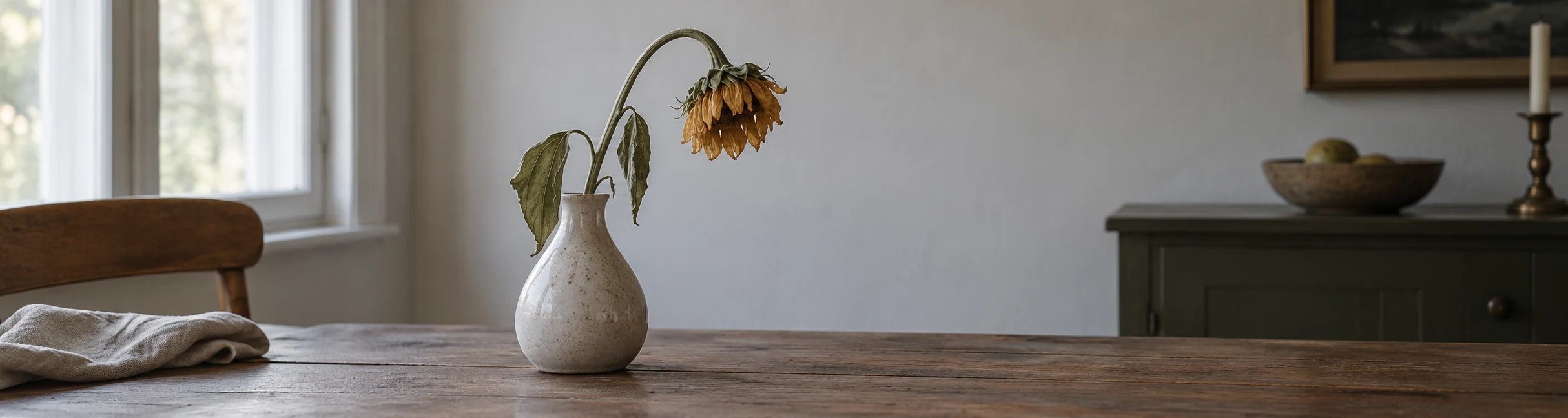 Verwelkte Sonnenblume hängt in einer Keramikvase auf einem rustikalen Holztisch.