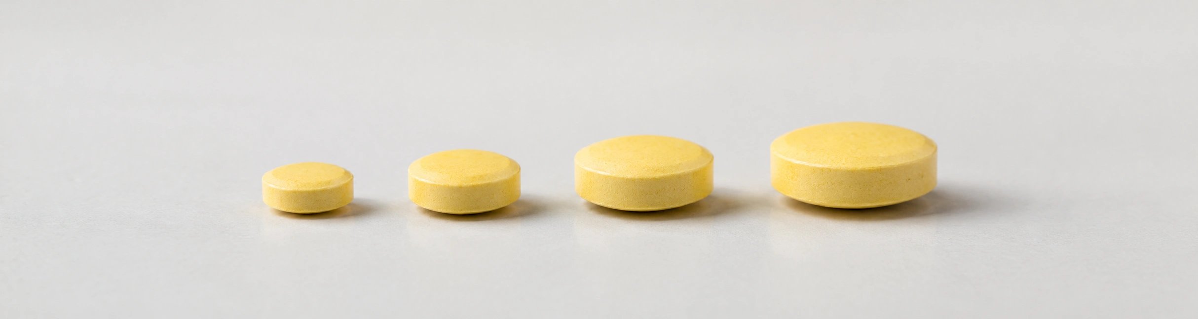 4 gleiche gelbe Tabletten nebeneinander in unterschiedlicher Größe