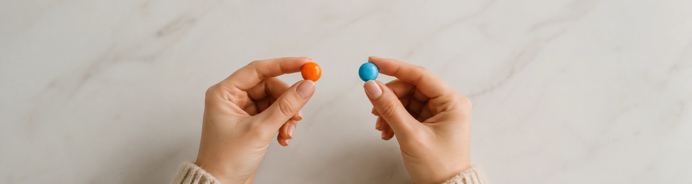 Kvinnliga händer håller en orange och en blå karamell mot en neutral bakgrund