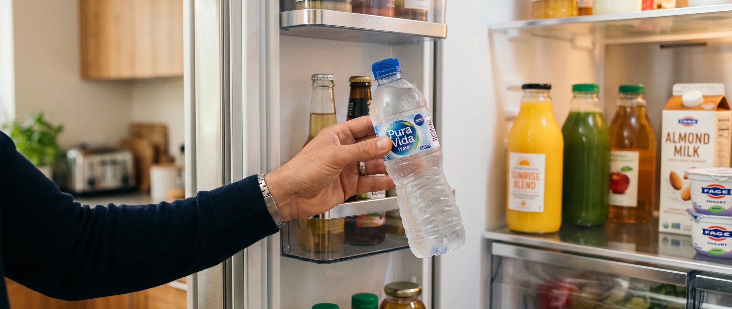Ein Mann nimmt eine Flasche Wasser aus dem K&uuml;hlschrank