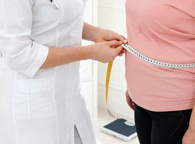 Eine Ärztin misst in einer Klinik die Taille einer übergewichtigen Frau mit einem Maßband