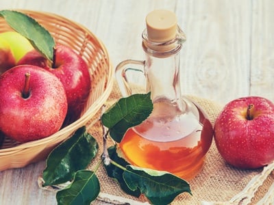 Eine Flasche Apfelessig mit einem Korb frischer Äpfel