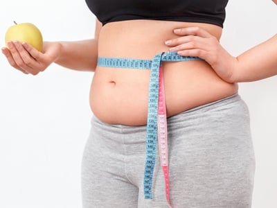 Eine Frau, die ihre Taille mit einem Maßband misst, während sie einen frischen grünen Apfel in der Hand hält