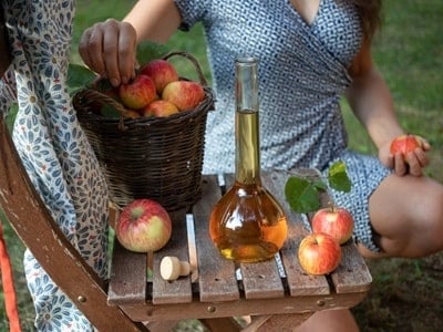 Eine Flasche Apfelessig in einem Garten, mit einer Frau im Hintergrund
